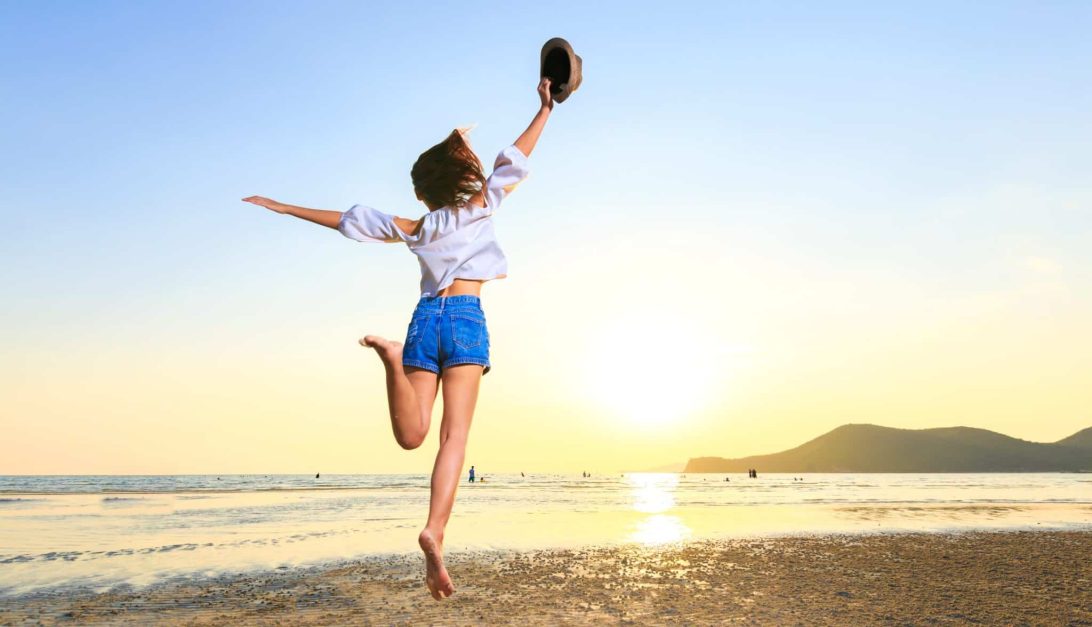 Au Pair travel women hold hat and jump on the beach.